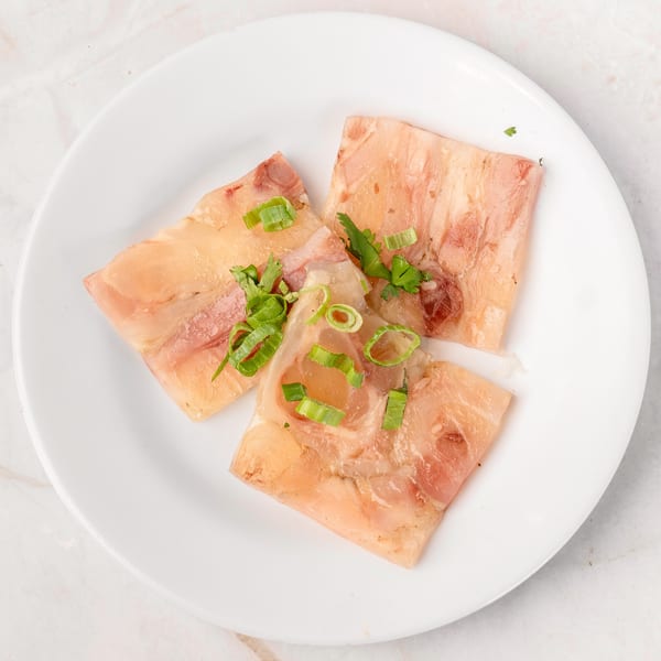 Three slices of translucent meat jelly, garnished with fresh green onions and cilantro, on a white plate.