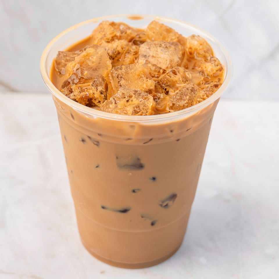 Iced coffee with milk and ice cubes in a clear plastic cup on a white marble surface.