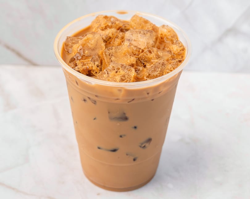 Iced coffee with milk and ice cubes in a clear plastic cup on a white marble surface.