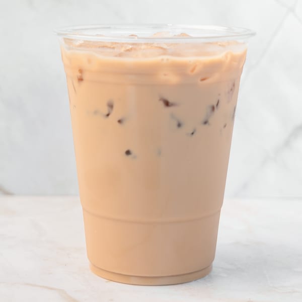 Iced coffee with milk and ice in a clear plastic cup on a white marble surface.