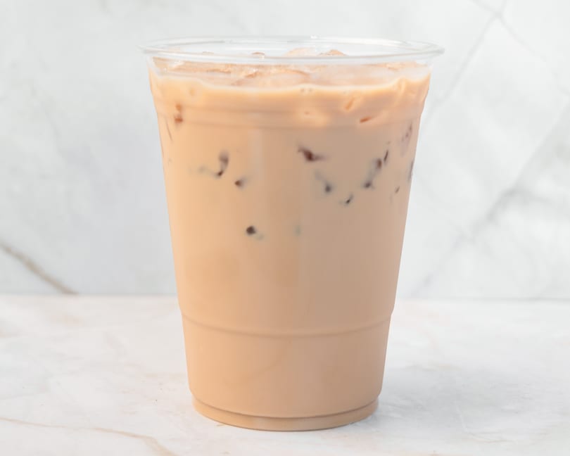 Iced coffee with milk and ice in a clear plastic cup on a white marble surface.
