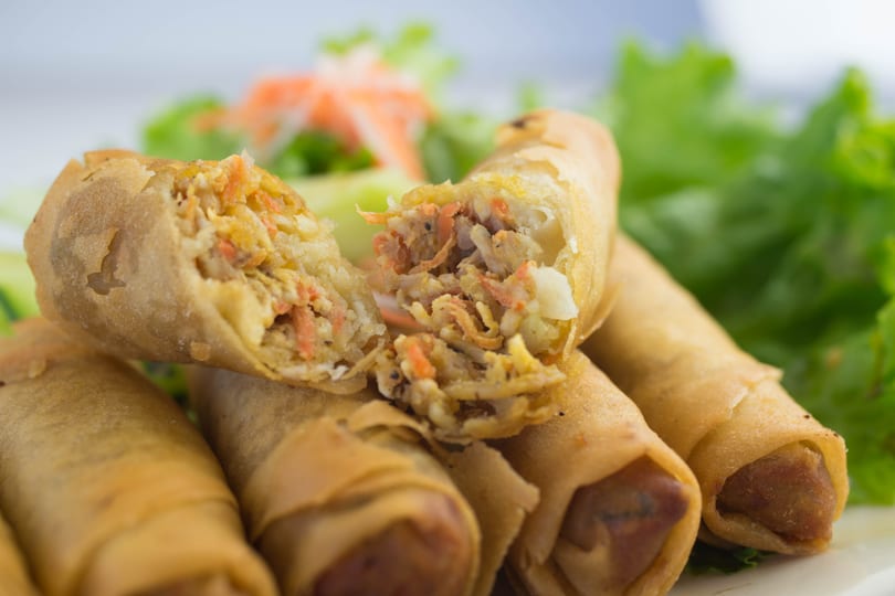 Crispy golden spring rolls, one cut open to reveal a savory filling of vegetables and meat, on a bed of lettuce.