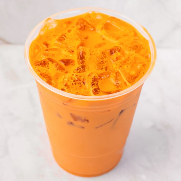 A vibrant orange Thai iced tea with ice in a clear plastic cup on a white marble surface.