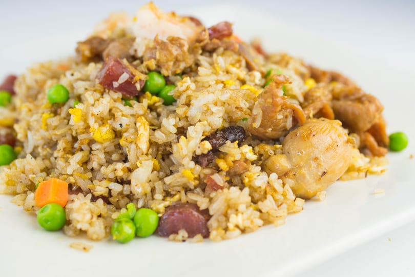 Close-up of fried rice with chicken, shrimp, peas, carrots, and sausage on a white plate.