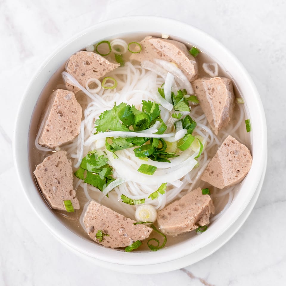 Top-down view of a bowl of Vietnamese pho with noodles, meat, cilantro, and green onions.