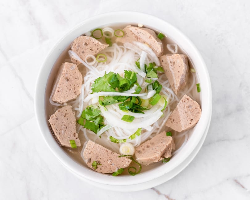 Top-down view of a bowl of Vietnamese pho with noodles, meat, cilantro, and green onions.