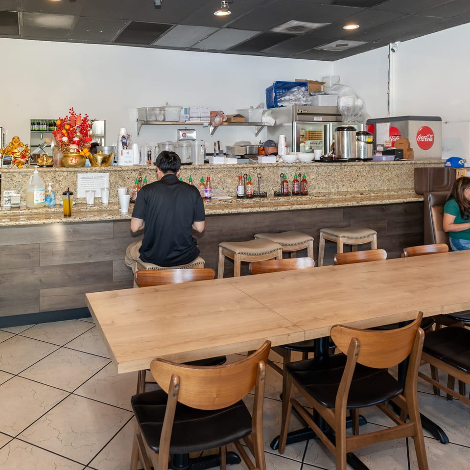 A restaurant interior with a customer at the counter, two women at a booth, and empty tables.