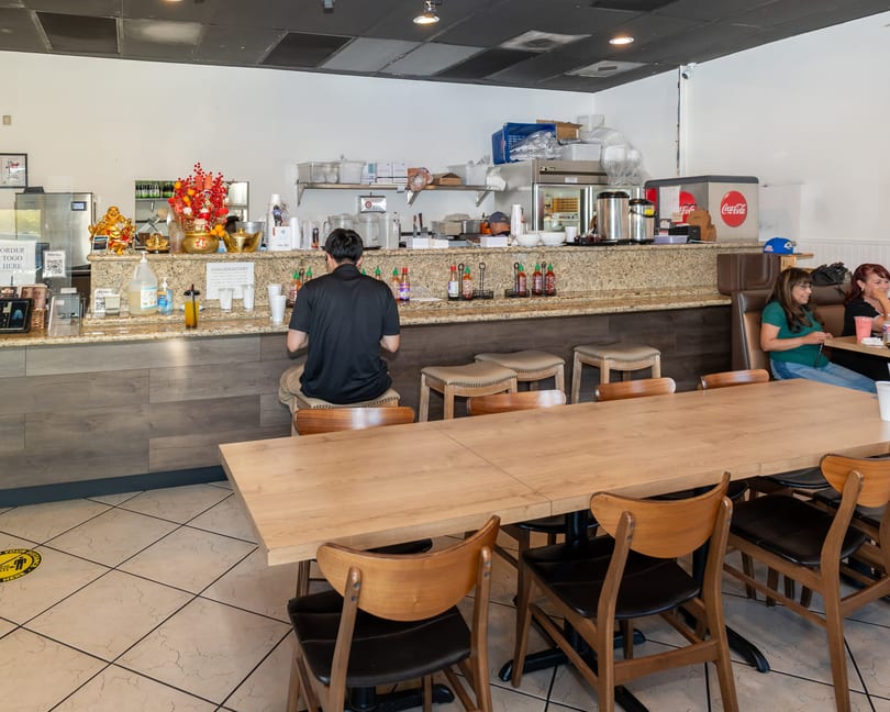 A restaurant interior with a customer at the counter, two women at a booth, and empty tables.