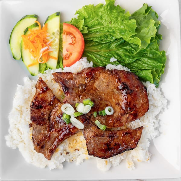 Grilled pork chops with rice, lettuce, tomato, cucumber, and pickled carrots on a white plate.