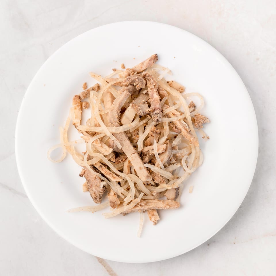 Top-down view of a white plate filled with shredded meat and thinly sliced onions.