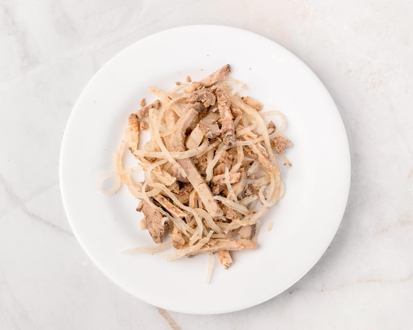 Top-down view of a white plate filled with shredded meat and thinly sliced onions.