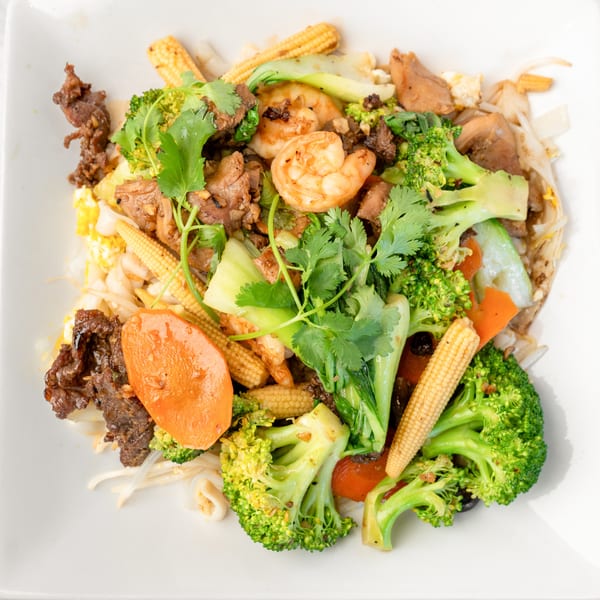 A colorful stir-fry with beef, shrimp, broccoli, baby corn, and carrots on a white plate.
