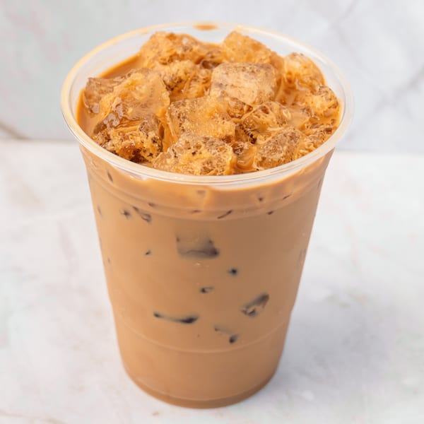 Iced coffee with milk and ice cubes in a clear plastic cup on a white marble surface.