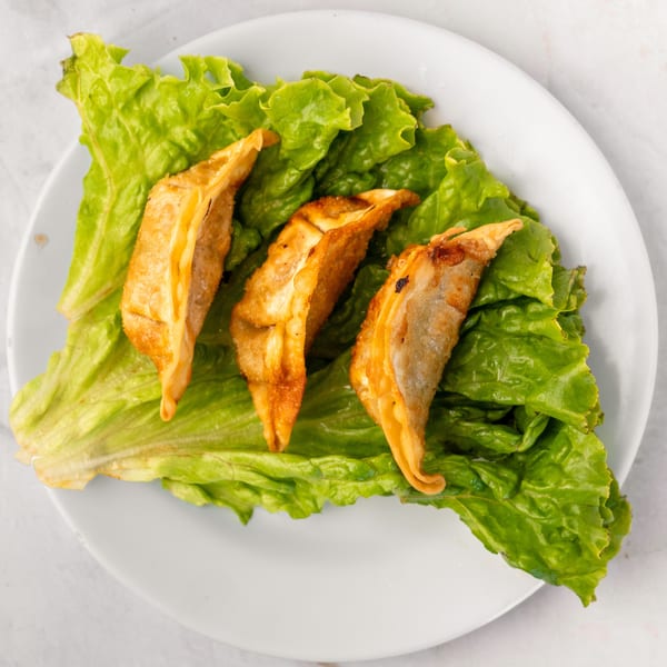 Three golden-brown fried dumplings rest on a bed of fresh green lettuce on a white plate.