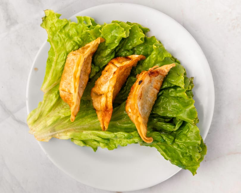 Three golden-brown fried dumplings rest on a bed of fresh green lettuce on a white plate.