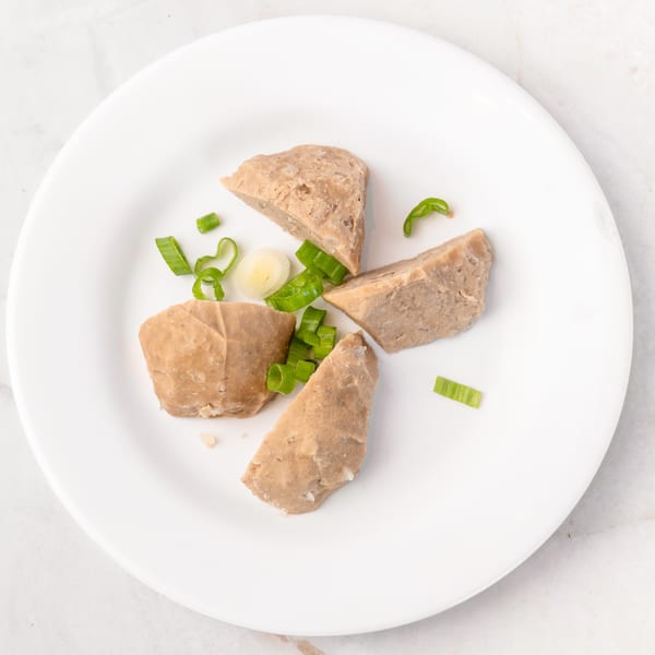 Four pieces of light brown meat, possibly meatballs, with chopped green onions and garlic on a white plate.