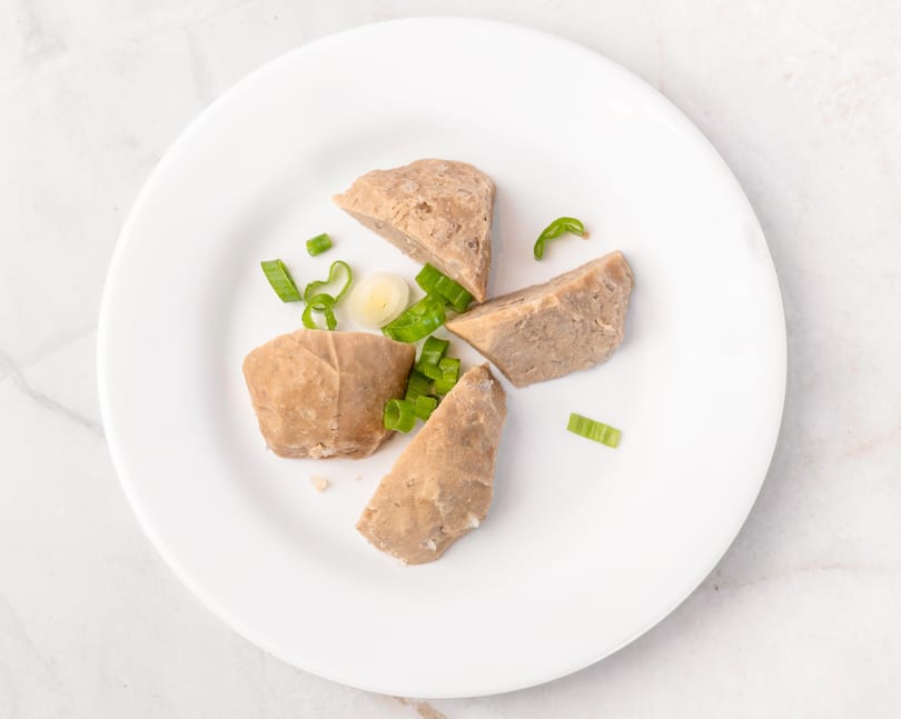 Four pieces of light brown meat, possibly meatballs, with chopped green onions and garlic on a white plate.