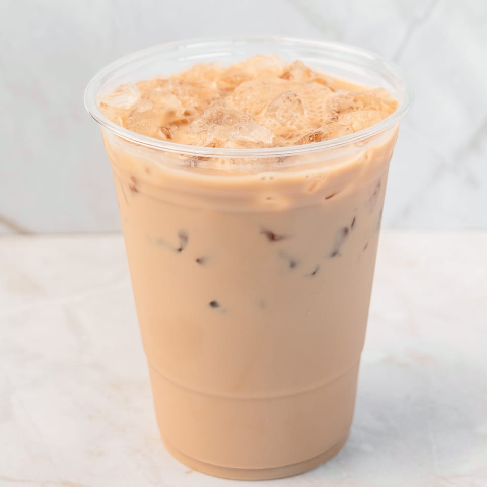 Iced coffee with milk and ice in a clear plastic cup on a white marble surface.