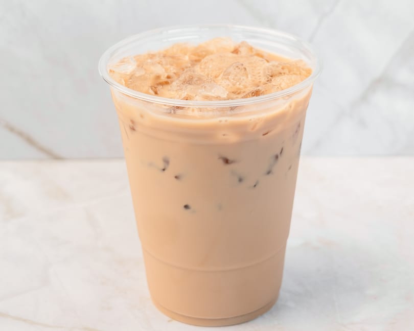Iced coffee with milk and ice in a clear plastic cup on a white marble surface.