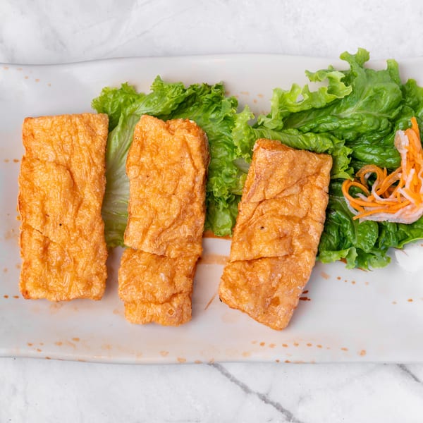 Three golden-brown fried tofu skin rolls with green lettuce and shredded carrots on a white plate.