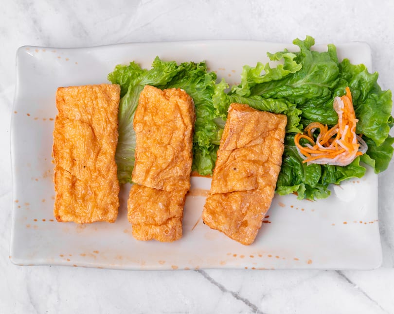 Three golden-brown fried tofu skin rolls with green lettuce and shredded carrots on a white plate.