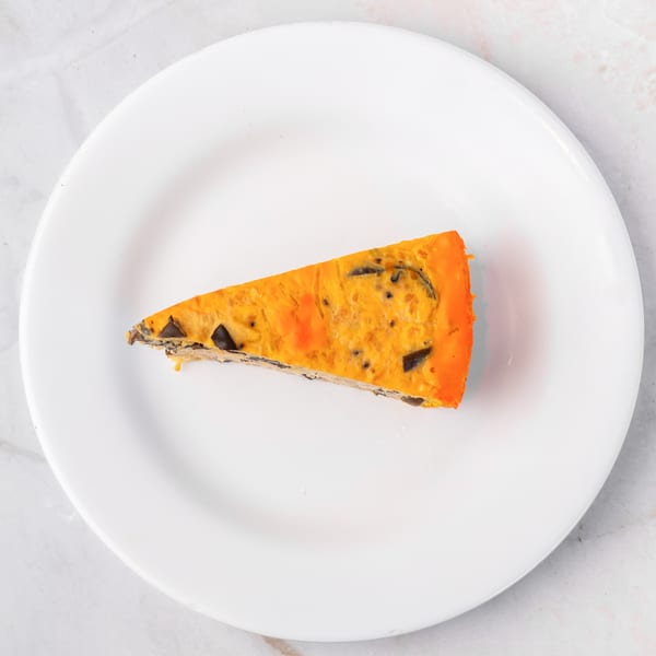 Slice of orange and brown quiche on a white plate, viewed from above.