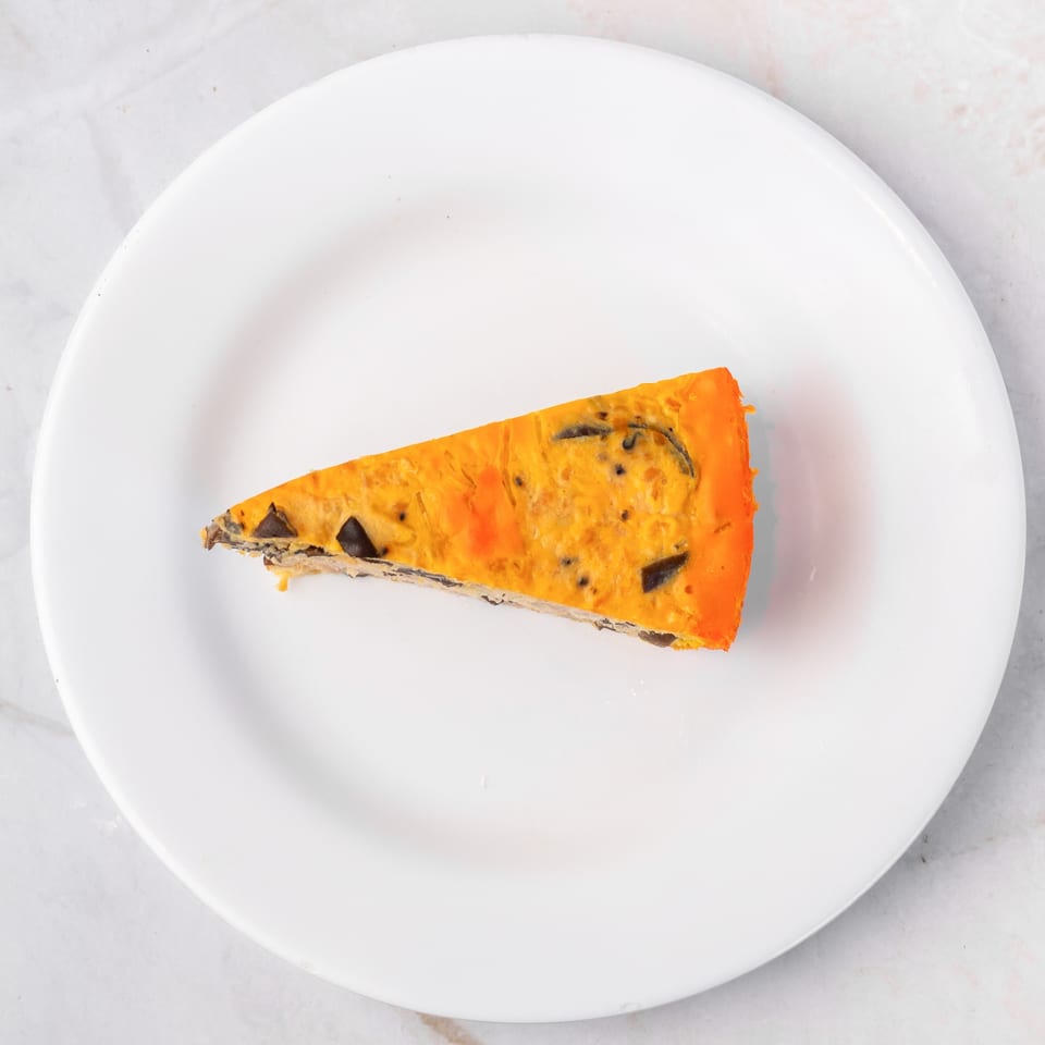 Slice of orange and brown quiche on a white plate, viewed from above.