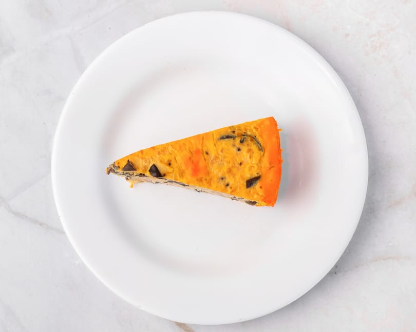 Slice of orange and brown quiche on a white plate, viewed from above.