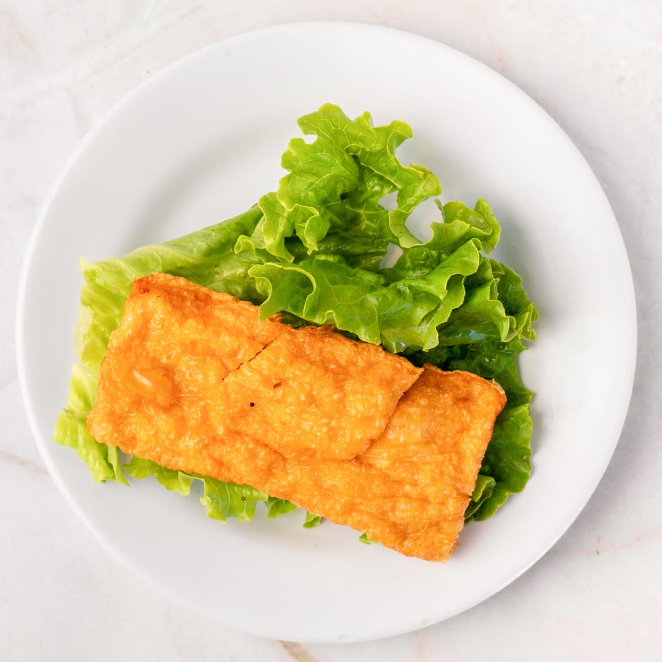 Golden fried tofu skin on a bed of fresh green lettuce, served on a white plate.