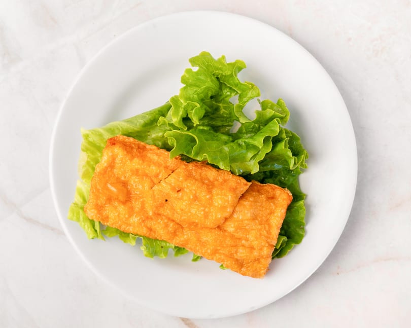 Golden fried tofu skin on a bed of fresh green lettuce, served on a white plate.
