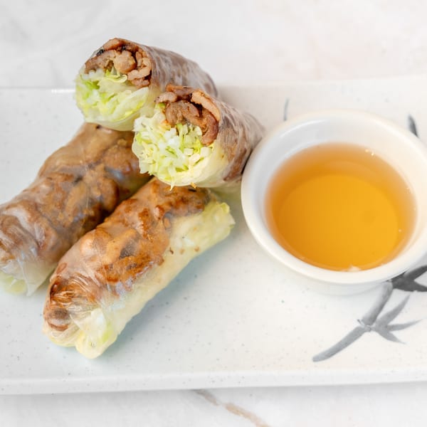 Three fresh spring rolls filled with meat and lettuce, served with a side of dipping sauce.