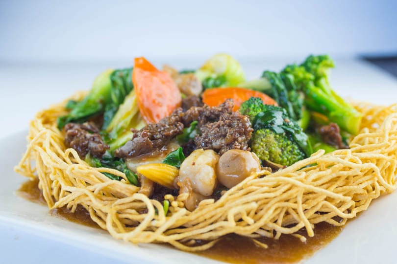Crispy noodles topped with beef, broccoli, carrots, baby corn, and mushrooms in a savory sauce.