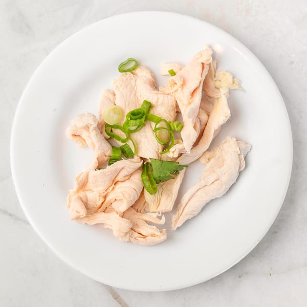 Shredded chicken breast with green onions and cilantro on a white plate.