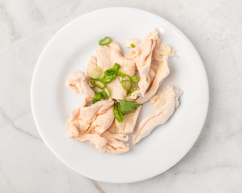 Shredded chicken breast with green onions and cilantro on a white plate.