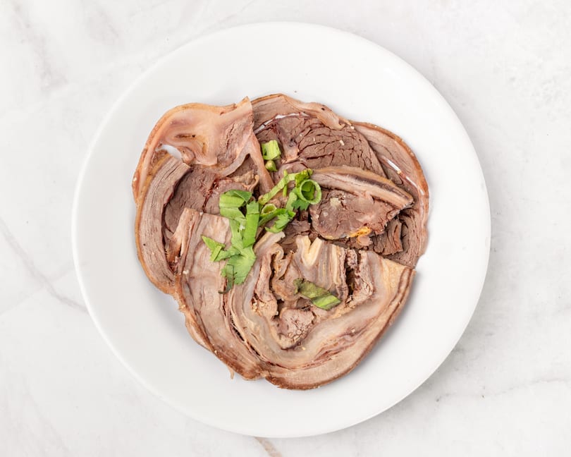 Thinly sliced beef and tripe, garnished with green onions and cilantro, on a white plate.
