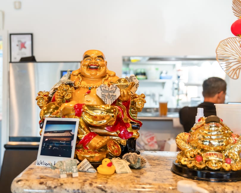 A golden Buddha statue with money and a polaroid on a counter, with a kitchen in the background.