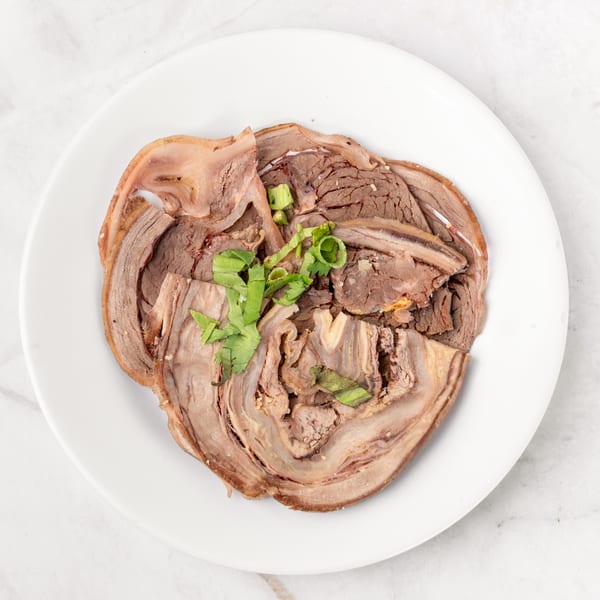 Thinly sliced beef and tripe, garnished with green onions and cilantro, on a white plate.