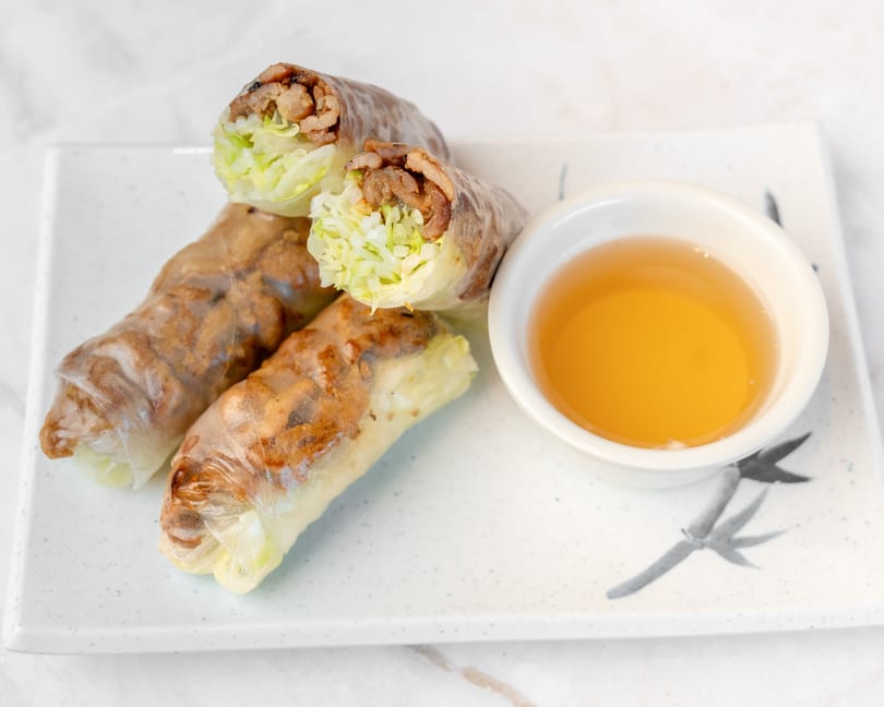 Three fresh spring rolls filled with meat and lettuce, served with a side of dipping sauce.