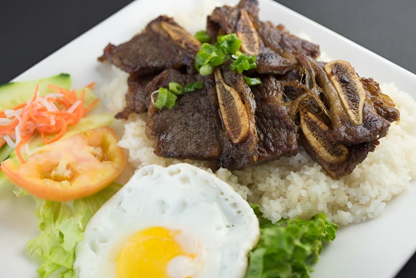 Grilled short ribs over white rice, with a fried egg, lettuce, tomato, and pickled vegetables.