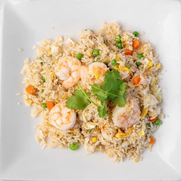 Shrimp fried rice with peas, carrots, and scrambled egg, garnished with cilantro on a white plate.
