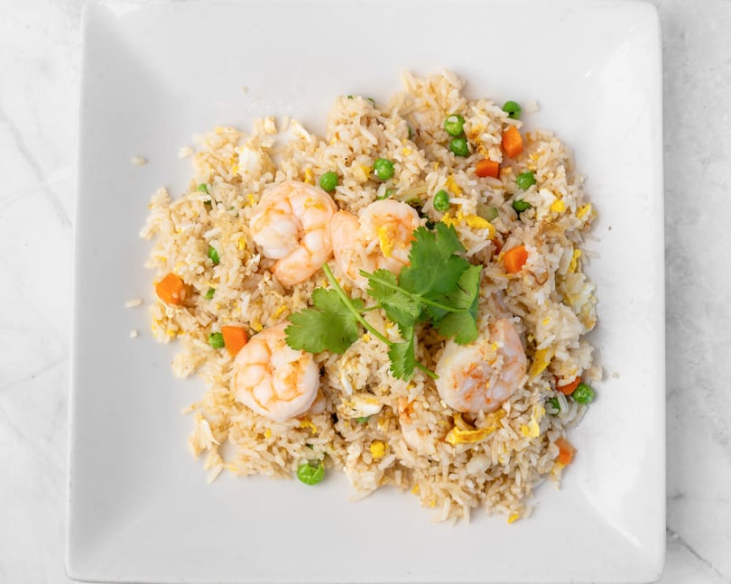 Shrimp fried rice with peas, carrots, and scrambled egg, garnished with cilantro on a white plate.
