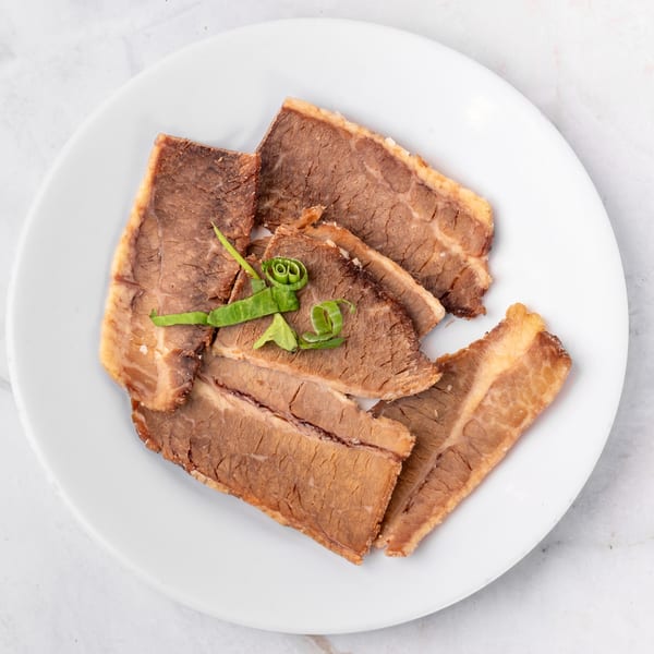 Slices of cooked beef brisket with green onions on a white plate.