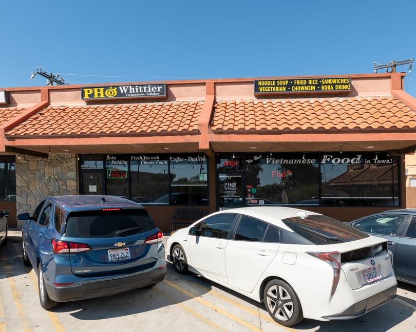 Pho Whittier Vietnamese Cuisine restaurant exterior with cars parked in front on a sunny day.