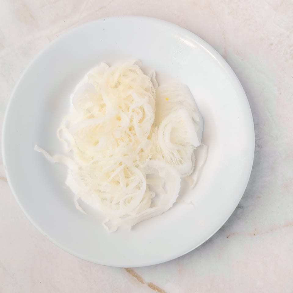 A white plate filled with thinly sliced, light-colored tripe, ready to be cooked.