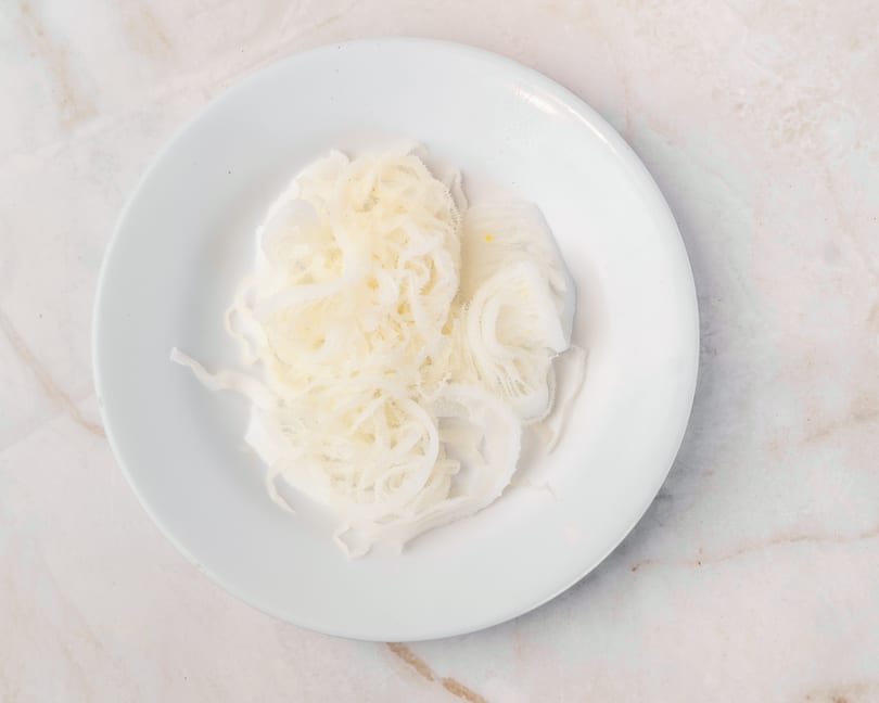A white plate filled with thinly sliced, light-colored tripe, ready to be cooked.