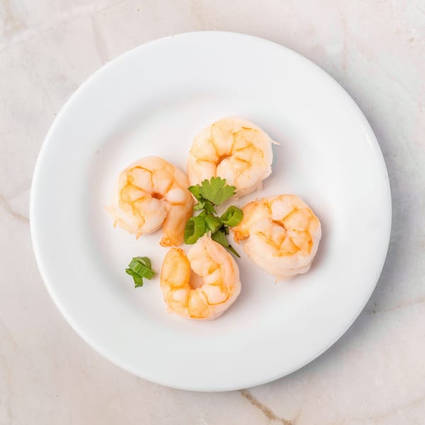 Four cooked shrimp with cilantro and green onions on a white plate.