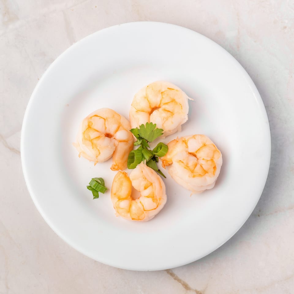 Four cooked shrimp with cilantro and green onions on a white plate.