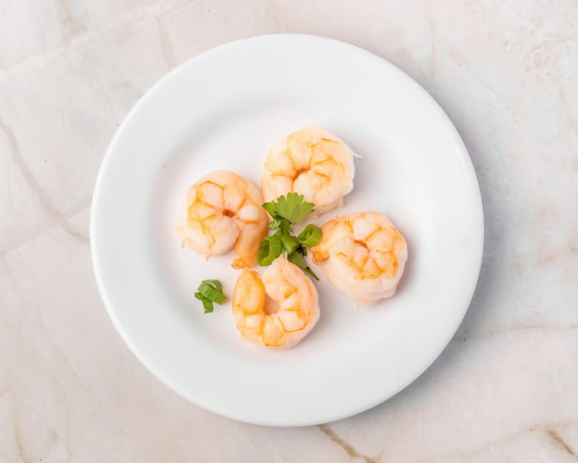 Four cooked shrimp with cilantro and green onions on a white plate.