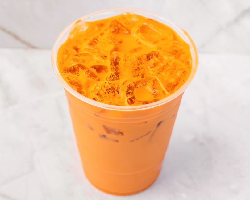 Iced Thai tea with ice cubes in a clear plastic cup on a white marble surface.