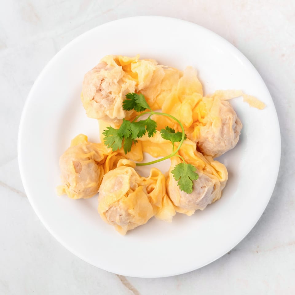 A white plate holds several steamed wontons, garnished with fresh green cilantro.